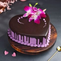 Heart‑shaped chocolate cake glazed in ganache and topped with fresh purple orchid blooms and edible gold accents.