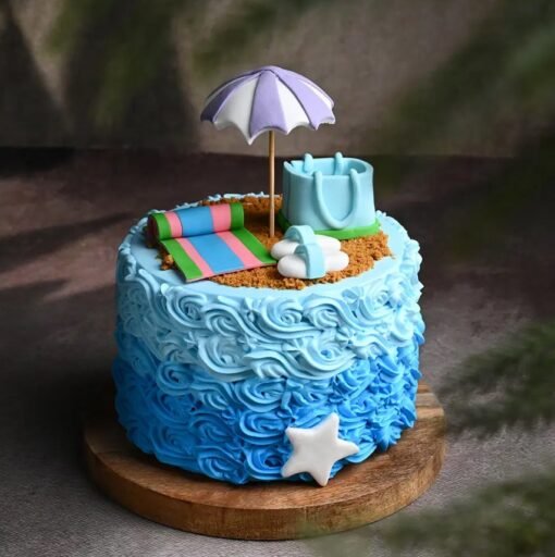 Fondant beach-themed cake with edible sand, umbrellas, sea waves, slippers, and tropical decorations for a summer celebration.