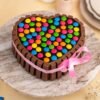 Heart‑shaped chocolate cake surrounded by KitKat bars, topped with Cadbury Gems candies and tied with a red ribbon.