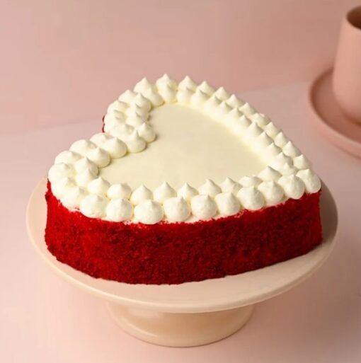Heart‑shaped red velvet cake with smooth cream‑cheese frosting, red crumble edges, and a “Heartfelt Delight” plaque.