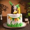 A jungle-themed fondant cake with a smiling monkey topper surrounded by leaves, trees, and safari elements.