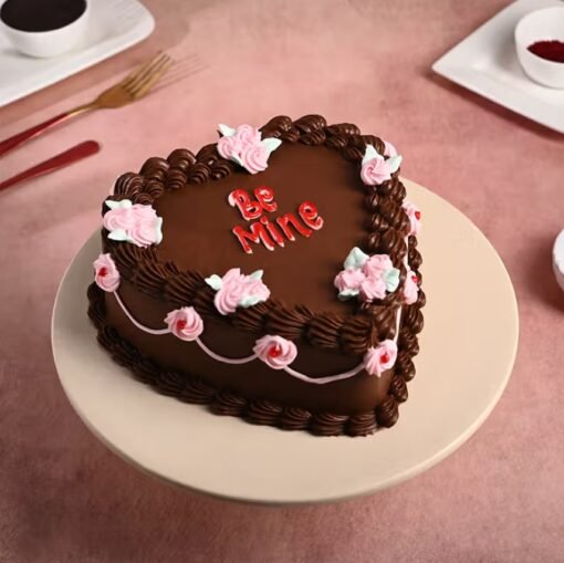Heart‑shaped chocolate cake glazed in shiny ganache, decorated with red hearts and a “Be Mine” topper.